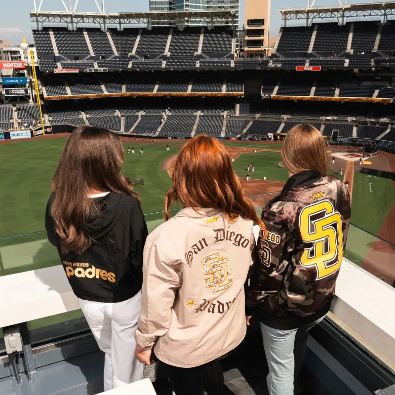 Three women in Padres jackets overlooking stadium
